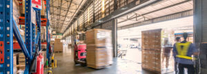 Full warehouse with forklift moving a pallet near an open garage door.